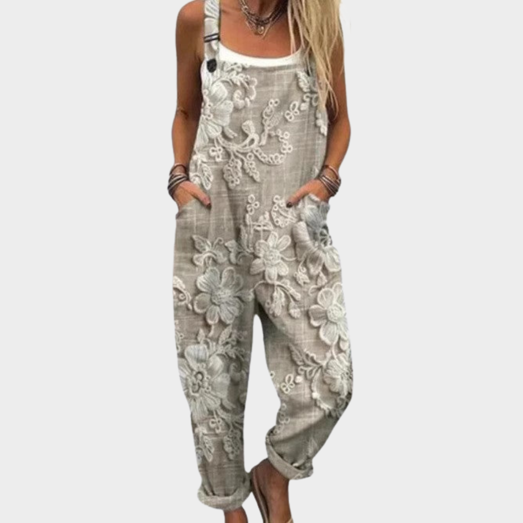 Woman wearing beige-grey overalls with a subtle tone-on-tone floral print, adjustable straps, elegant and relaxed.