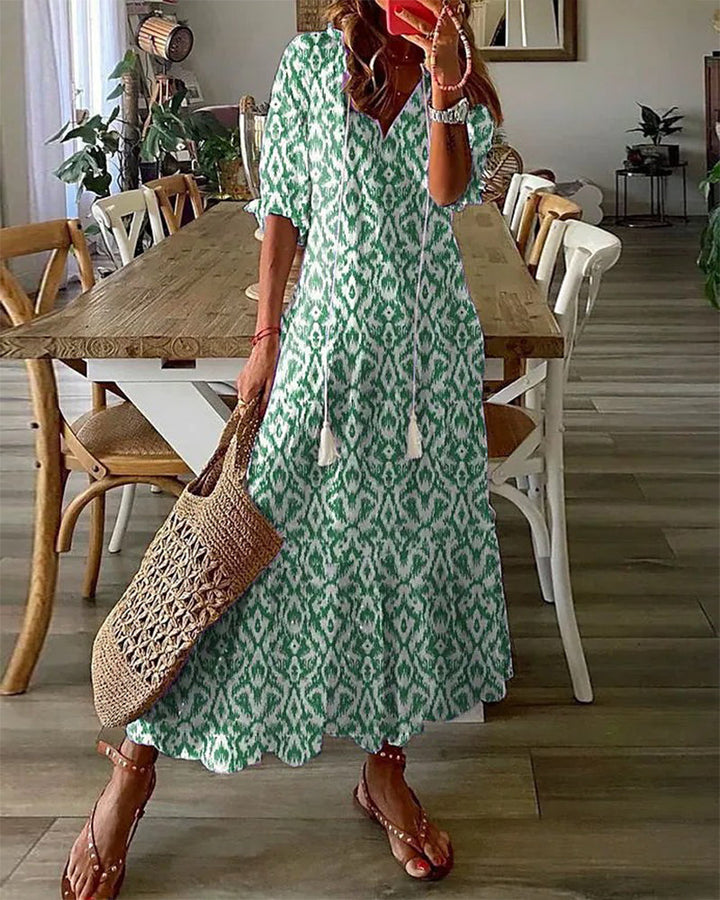 Woman wearing the Jacqueline™ boho maxi dress with fringe details and a V-neckline, relaxed in a warm outdoor setting.