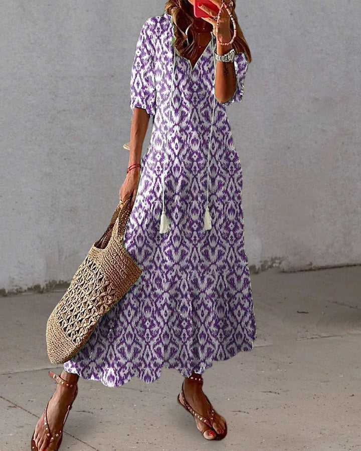 Woman wearing the Jacqueline™ boho maxi dress with fringe details and a V-neckline, relaxed in a warm outdoor setting.
