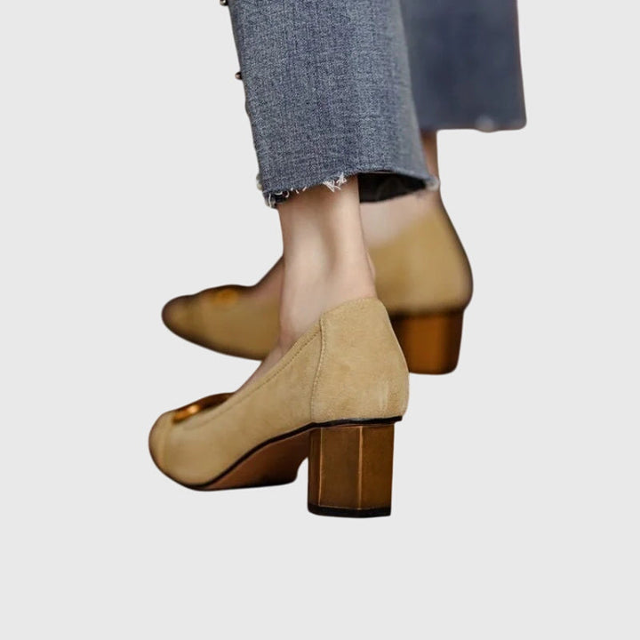 A woman wearing khaki block-heel court shoes with a gold buckle detail, standing with ease and confidence.