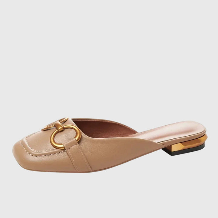 A cream closed-toe mule with a gold horsebit ring detail and a low heel.