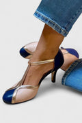 A woman wearing navy, blush and gold T-strap heels with a rounded toe, paired with jeans.