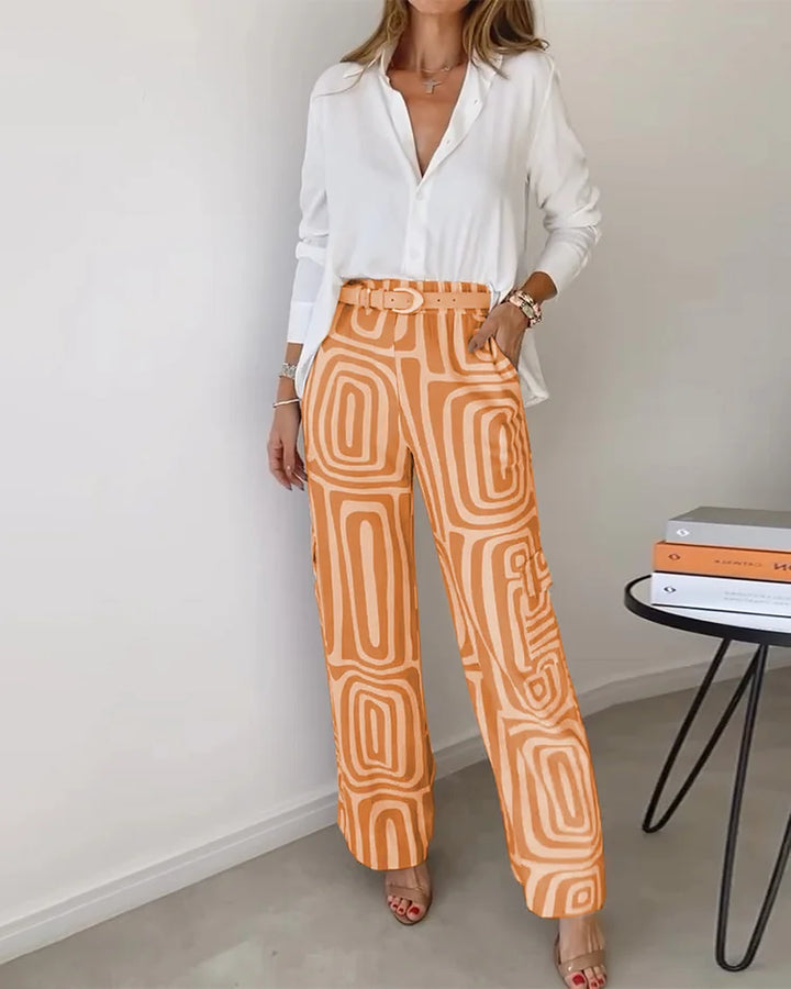 A woman wearing a plain button-up top with geometric-print pants and a belt at the waist.