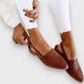 A woman wearing warm brown woven pointed-toe slingback flats with white cropped pants.