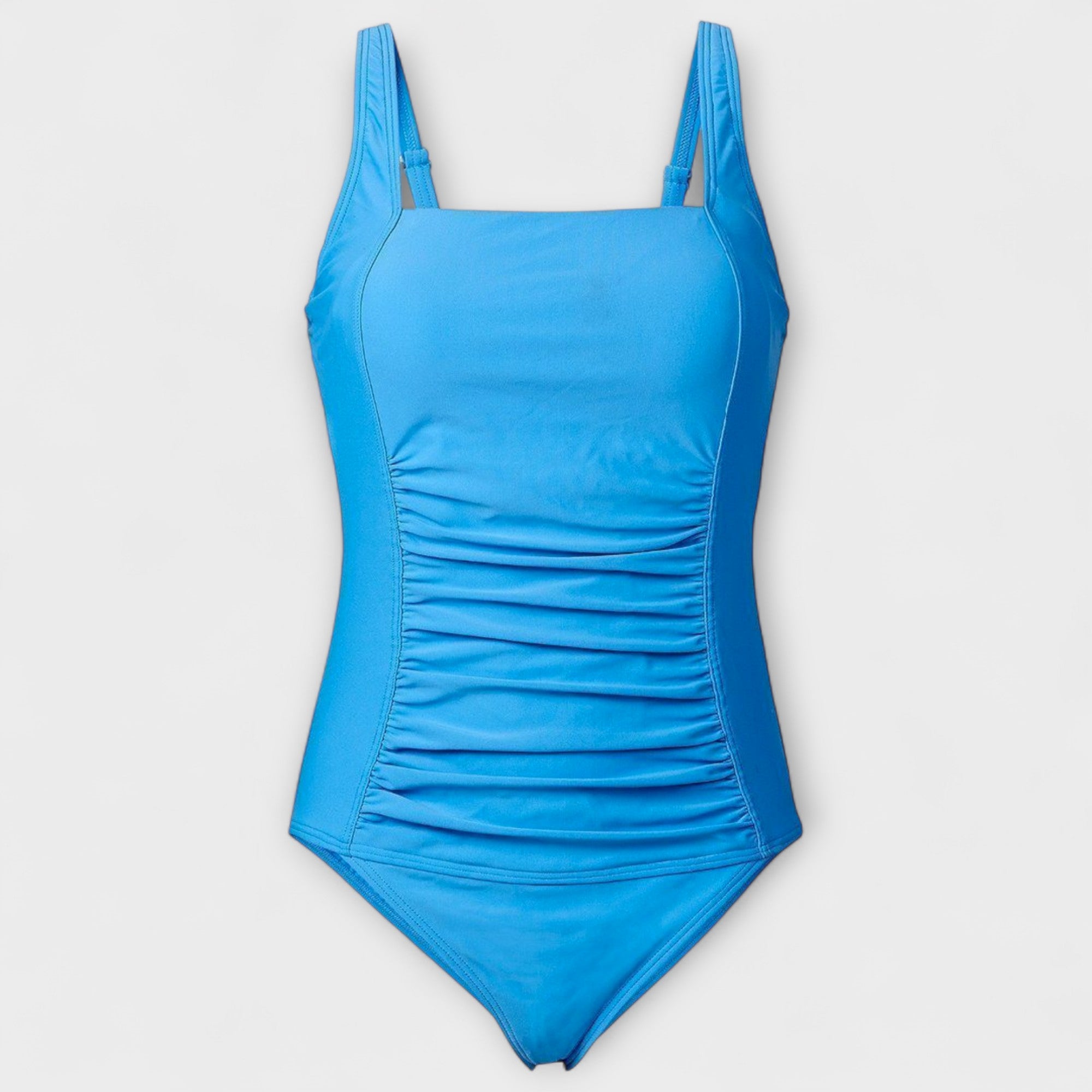 A woman on the sand in a retro-style padded swimsuit, poised and confident in the sunshine.