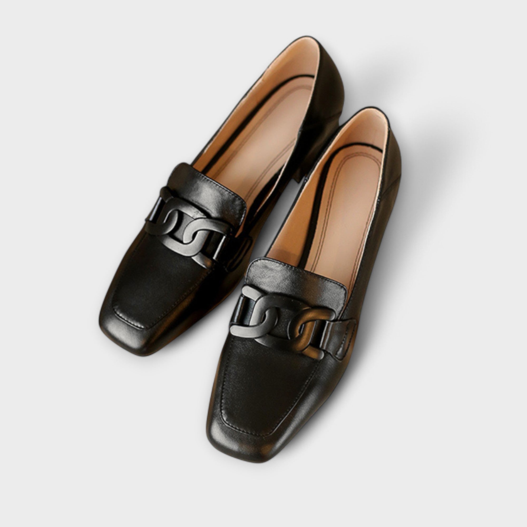A pair of soft beige square-toe loafers with a chain-link ornament across the front.