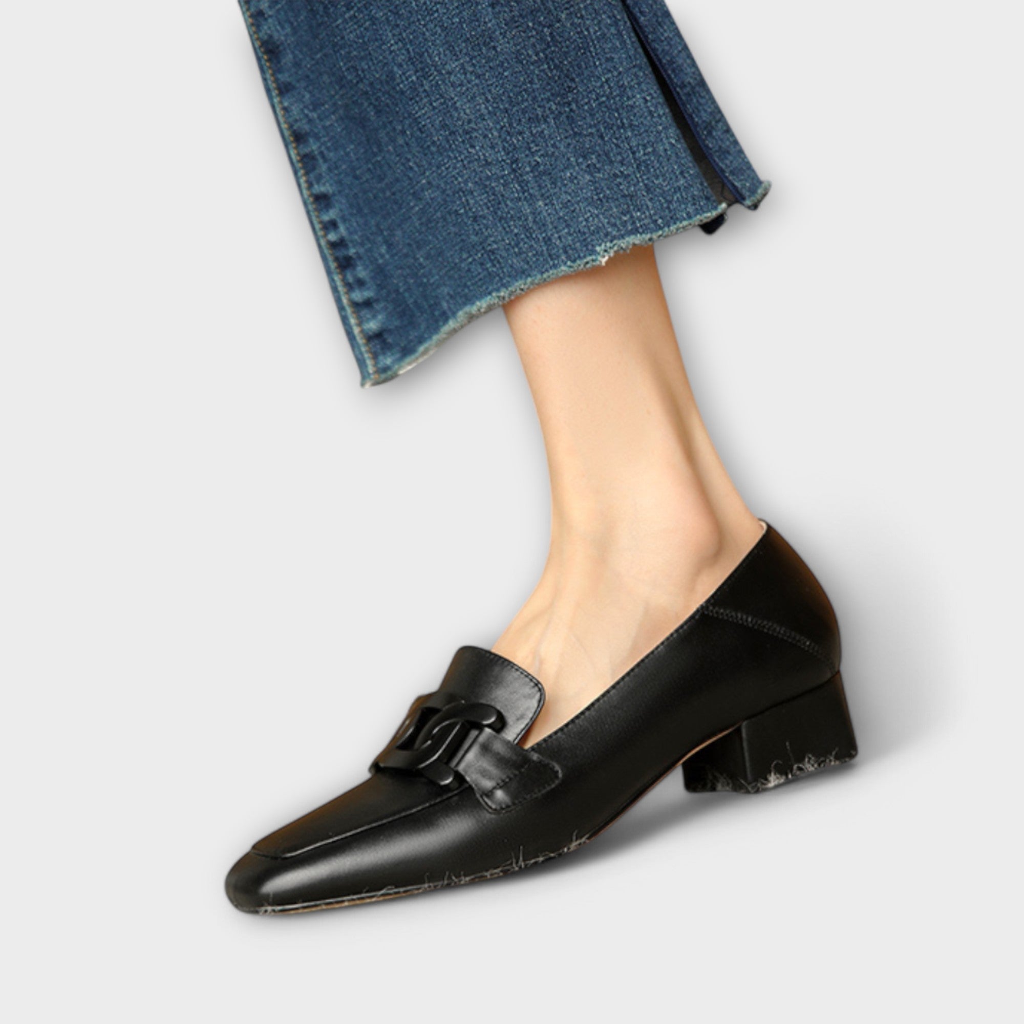 A pair of soft beige square-toe loafers with a chain-link ornament across the front.