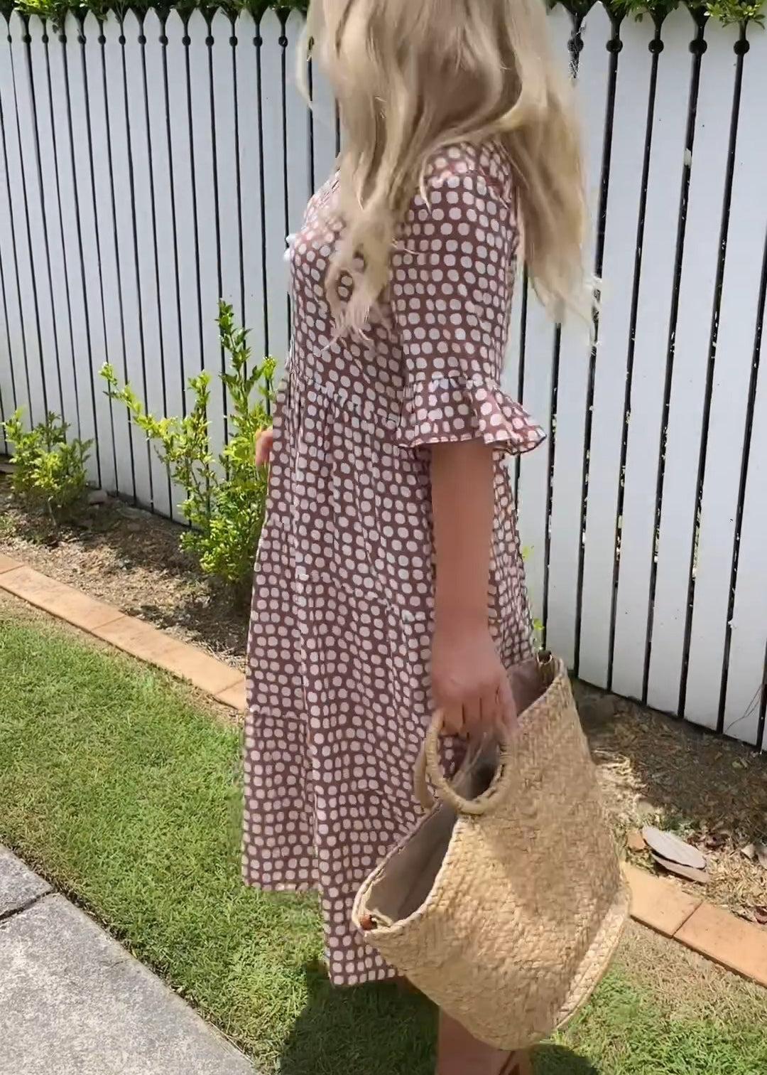Woman wearing the Natalie™ polka dot midi dress with short sleeves, relaxed and smiling in a summer setting.