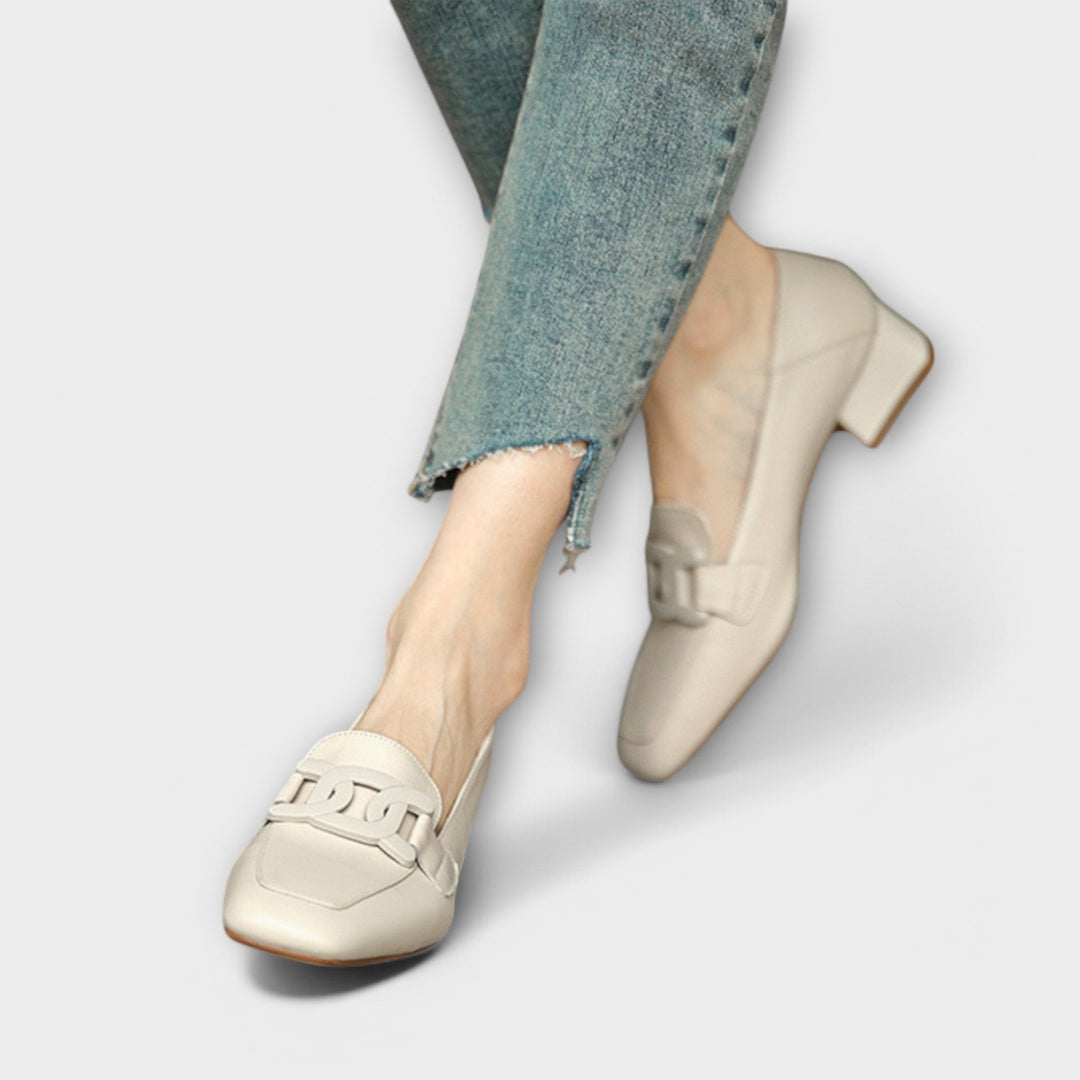 A pair of soft beige square-toe loafers with a chain-link ornament across the front.
