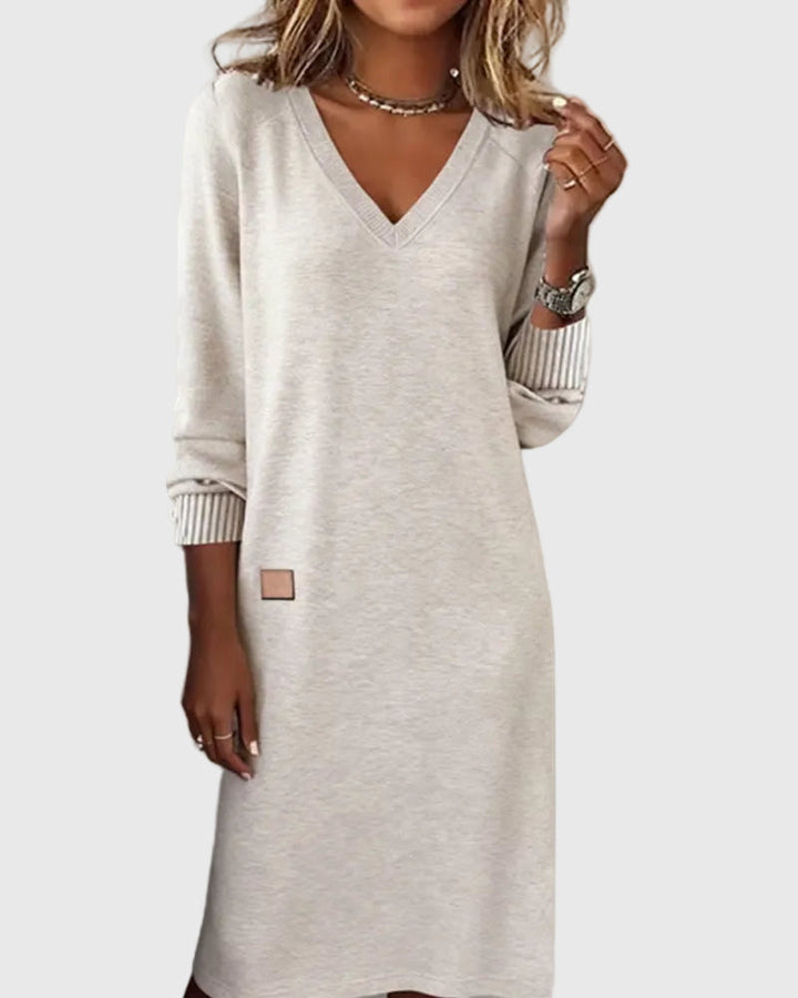 Woman wearing the Susan flowing elegant dress in beige, standing relaxed and smiling.