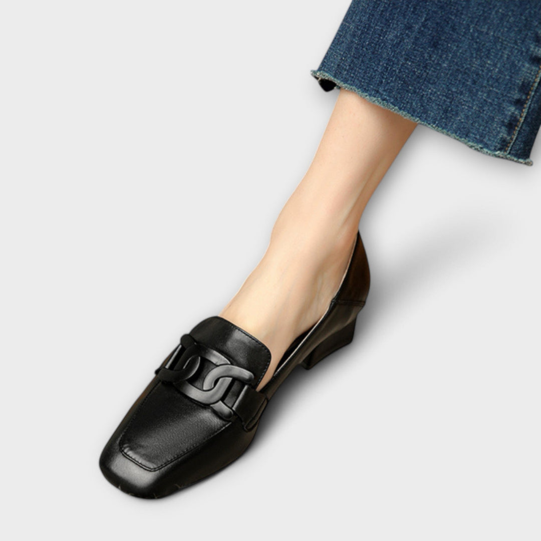 A pair of soft beige square-toe loafers with a chain-link ornament across the front.