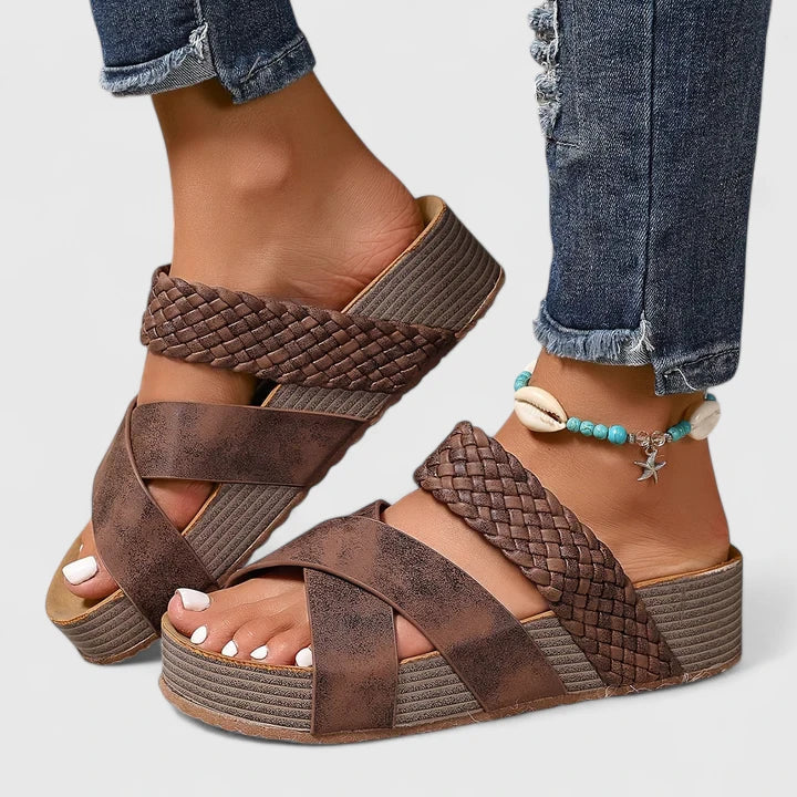 A woman strolling on a sunny street wearing beige woven comfort sandals with crossed straps.