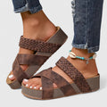 A woman strolling on a sunny street wearing beige woven comfort sandals with crossed straps.