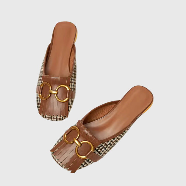 A cream closed-toe mule with a gold horsebit ring detail and a low heel.