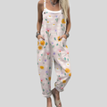 A woman wearing soft pink overalls printed with scattered daisies and wildflowers, smiling in a park.