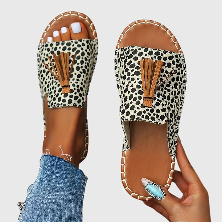 A woman wearing colourful patterned boho slides with tassel details on a holiday day out.