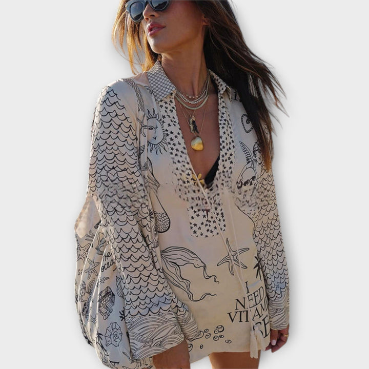 Woman walking on the beach in a relaxed tunic dress with playful maritime print and tie collar.