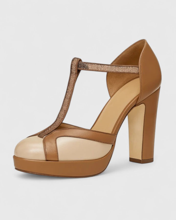 A woman wearing brown round-toe T-strap heels, standing elegantly in a smart outfit.