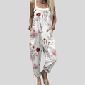Woman wearing white overalls printed with fine branches and red and burgundy blossoms, standing elegantly.
