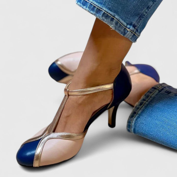 A woman wearing navy, blush and gold T-strap heels with a rounded toe, paired with jeans.