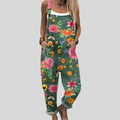 A woman wearing deep teal green overalls with a lush pink, orange and yellow floral print, smiling on a warm day.