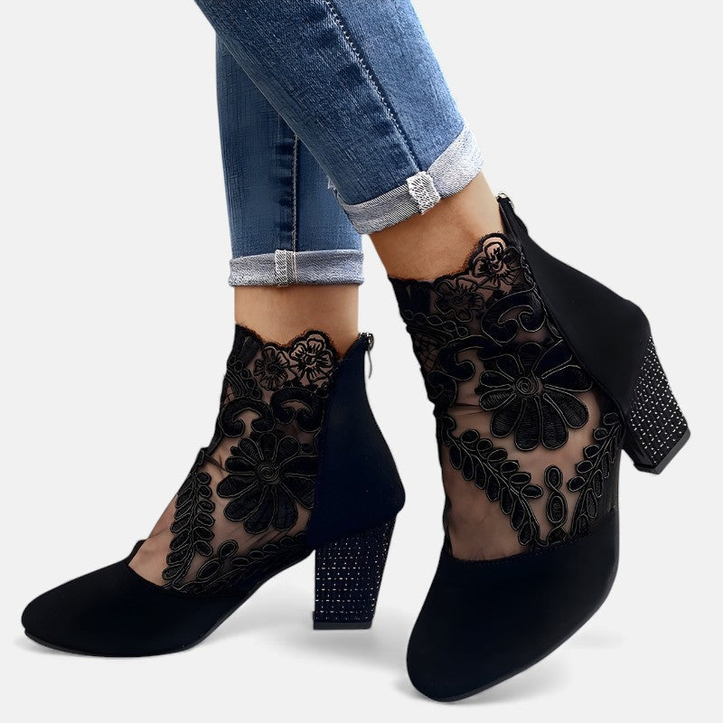A woman wearing wine block-heel shoes with a sheer black floral-lace ankle overlay and a crystal-set heel