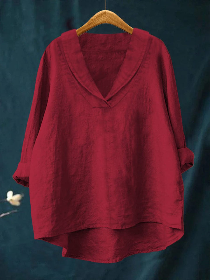 A woman wearing an elegant plain summer blouse with a flowing drape, styled with pants.
