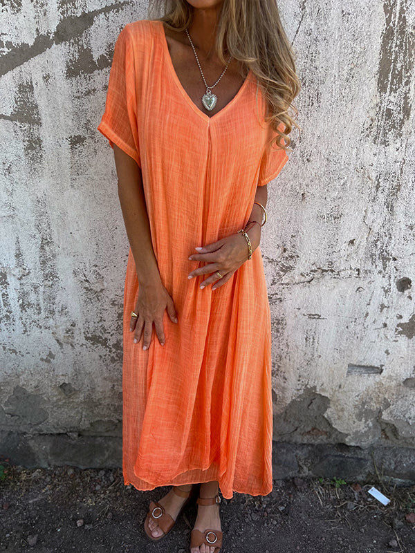 Woman wearing the Andrea™ flowing V-neck dress with short sleeves, standing relaxed in warm sunlight.
