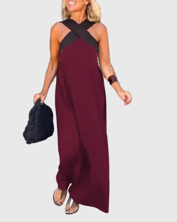 Woman wearing the Julie halterneck maxi dress in navy with a contrast crossover neckline, walking outdoors.