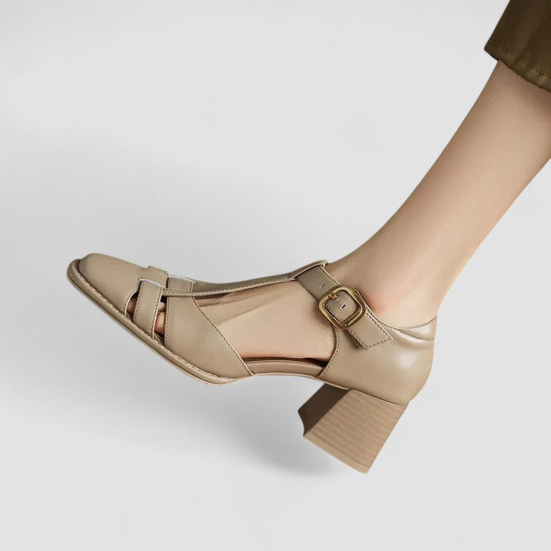 A woman wearing beige t-strap block heel sandals with an adjustable buckle, standing comfortably.