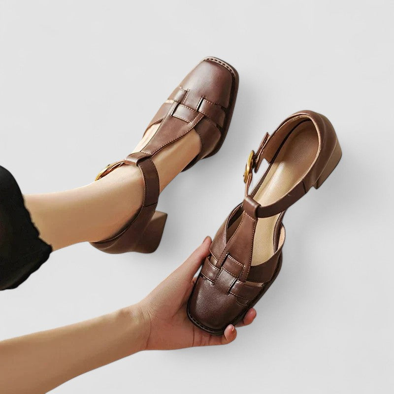 A woman wearing beige t-strap block heel sandals with an adjustable buckle, standing comfortably.