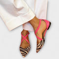 A woman wearing pointed flats with a zebra-print toe and pink cross-over ankle straps.