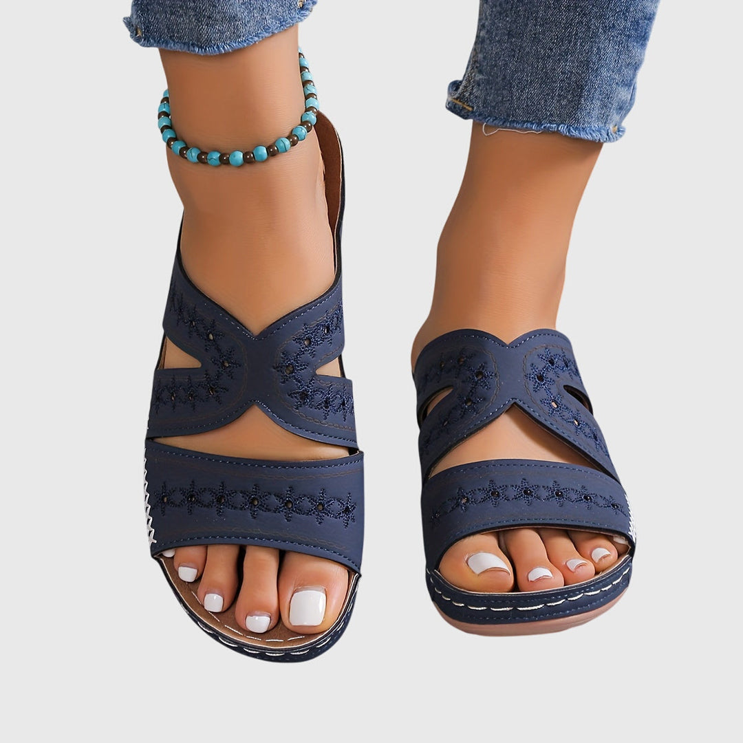 A woman walking gracefully in elegant wide-fit support sandals with an open-front design.