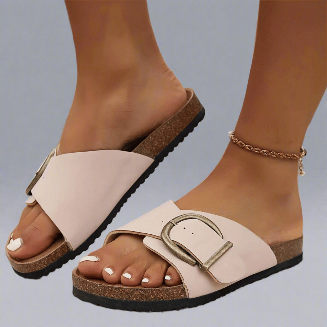 A woman wearing minimalist buckle slip-on sandals with a wide crossover strap on a summer evening.