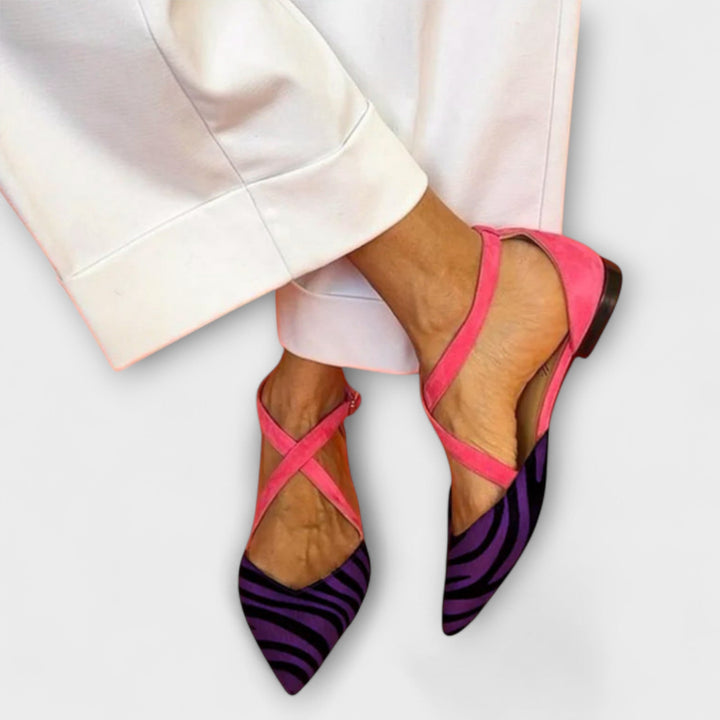 A woman wearing pointed flats with a zebra-print toe and pink cross-over ankle straps.