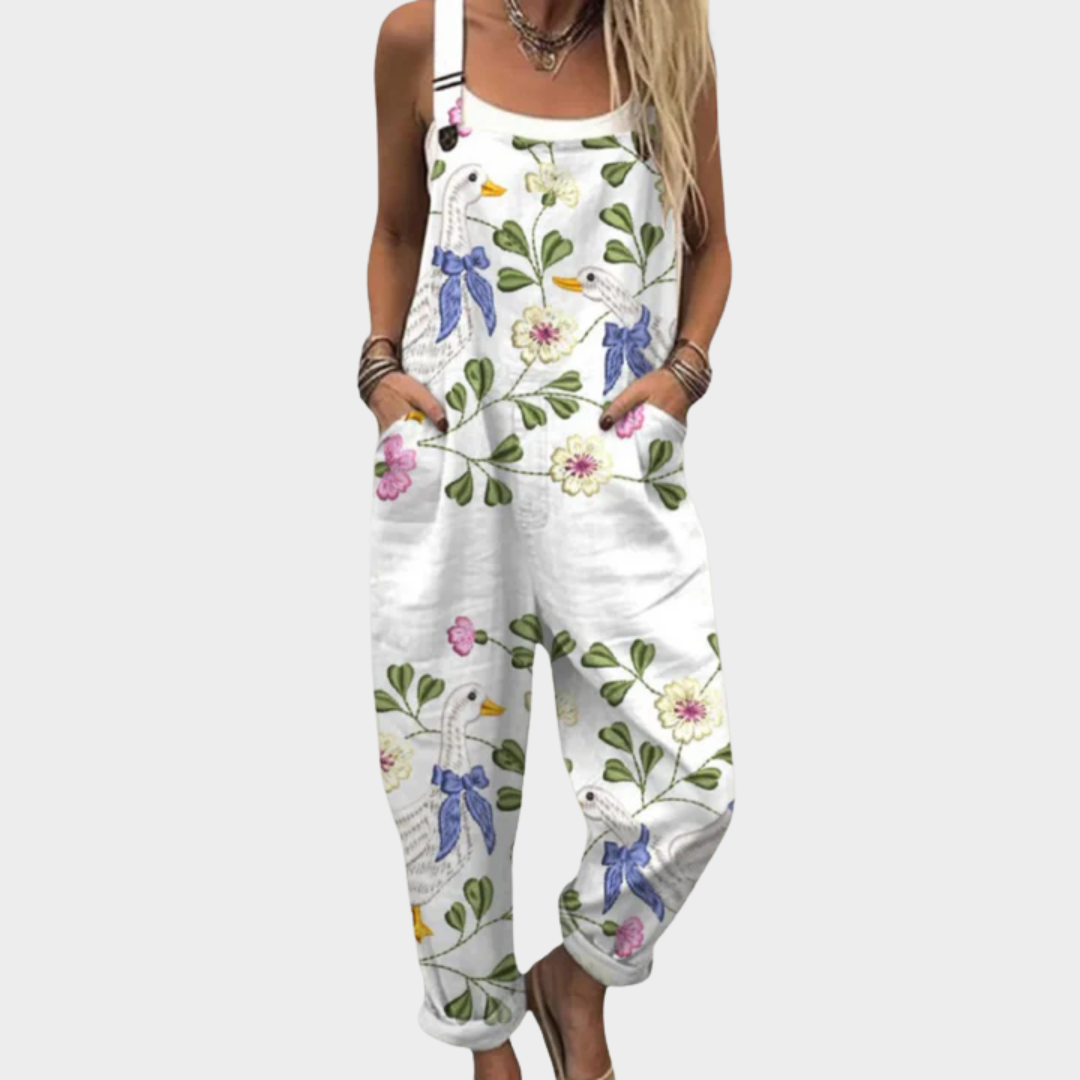 Woman wearing white overalls printed with geese in blue bows among green leaves and blooms, adjustable straps, cheerful and relaxed.