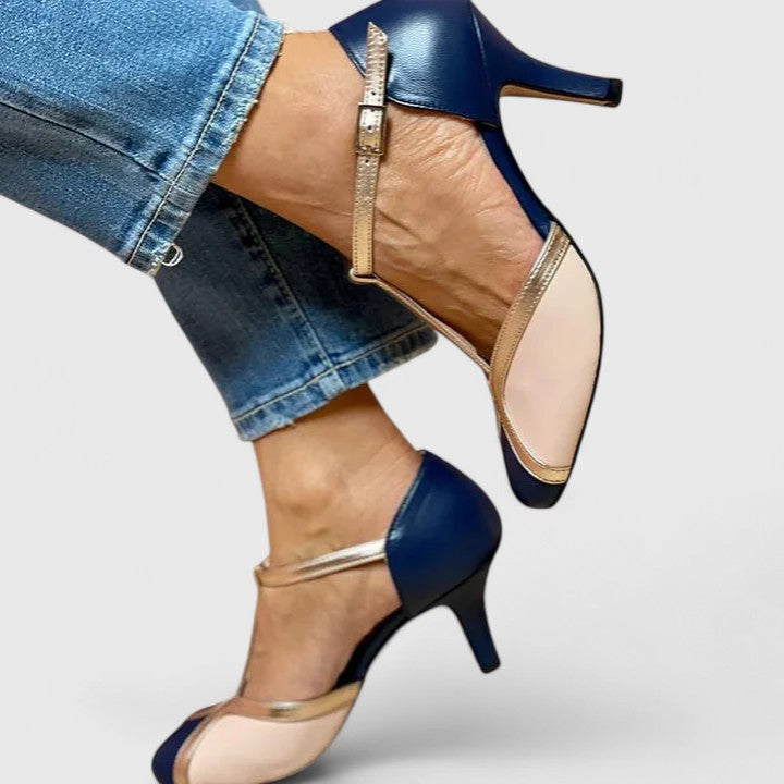 A woman wearing navy, blush and gold T-strap heels with a rounded toe, paired with jeans.