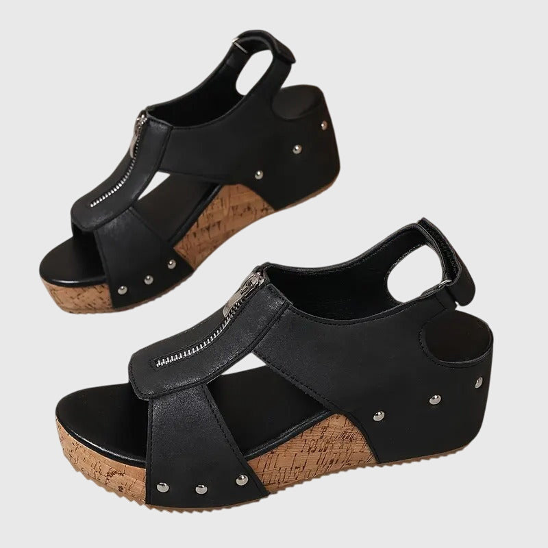 A woman wearing black zip-front wedge sandals with a cushioned footbed and open toe.