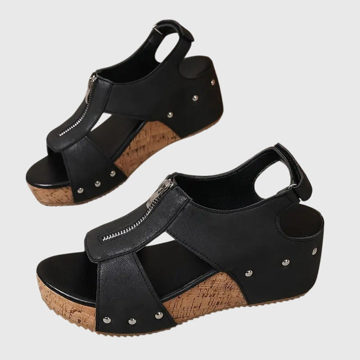 A woman wearing black zip-front wedge sandals with a cushioned footbed and open toe.