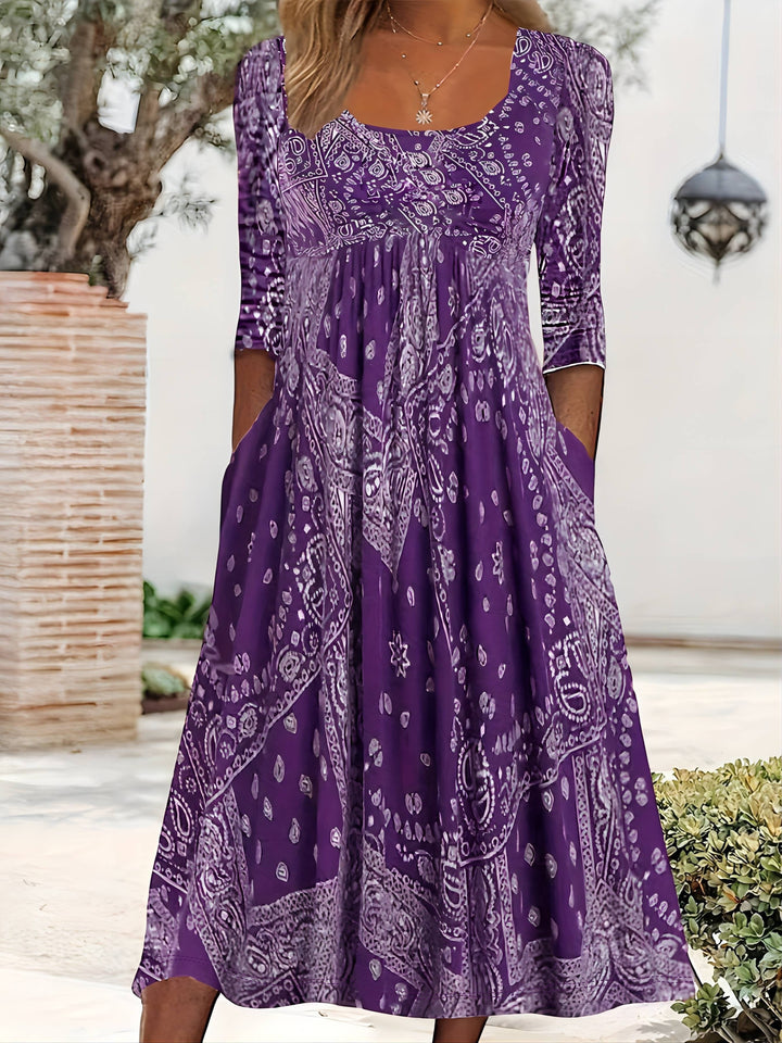 A woman wearing the Maria long sleeve grey paisley midi dress with a square neckline and flowing skirt, styled for a relaxed day out.
