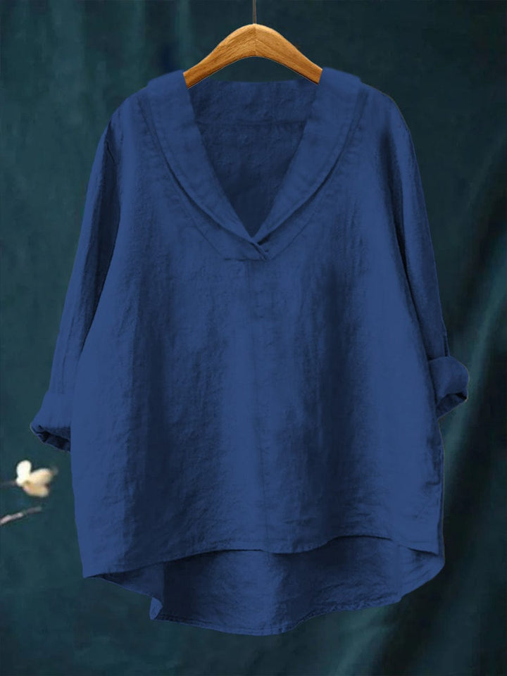 A woman wearing an elegant plain summer blouse with a flowing drape, styled with pants.