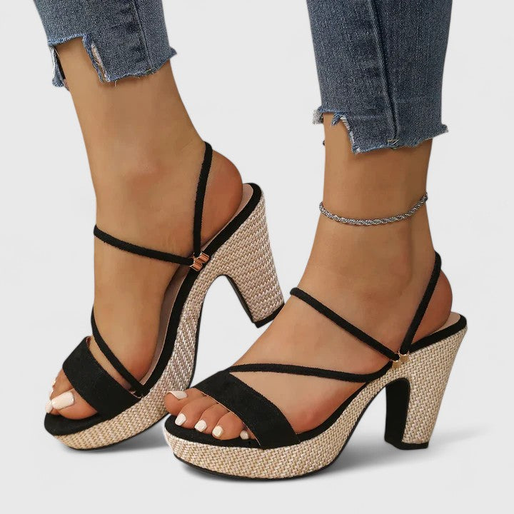 A woman wearing black adjustable strappy heels, standing gracefully in an elegant outfit.