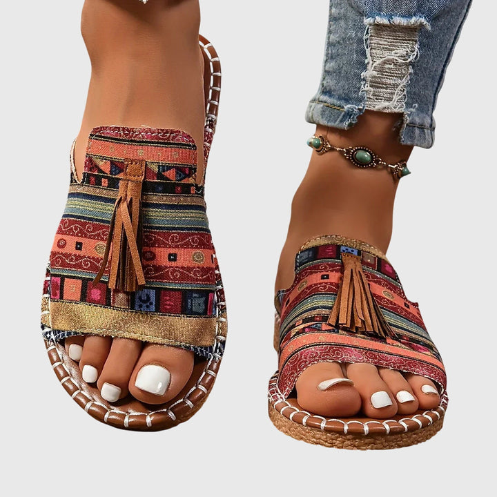 A woman wearing colourful patterned boho slides with tassel details on a holiday day out.