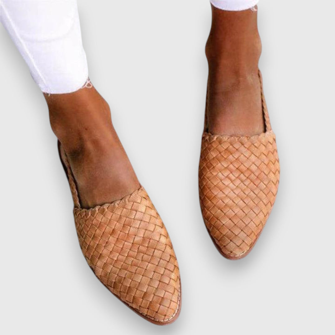 A woman wearing warm brown woven pointed-toe slingback flats with white cropped pants.
