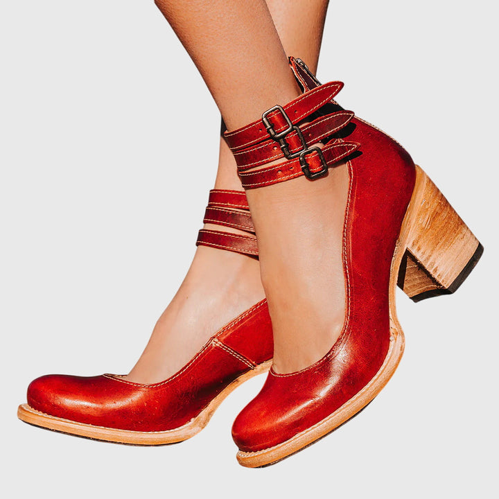 A woman wearing tan block-heel court shoes with buckled ankle straps, walking gracefully in a refined outfit.