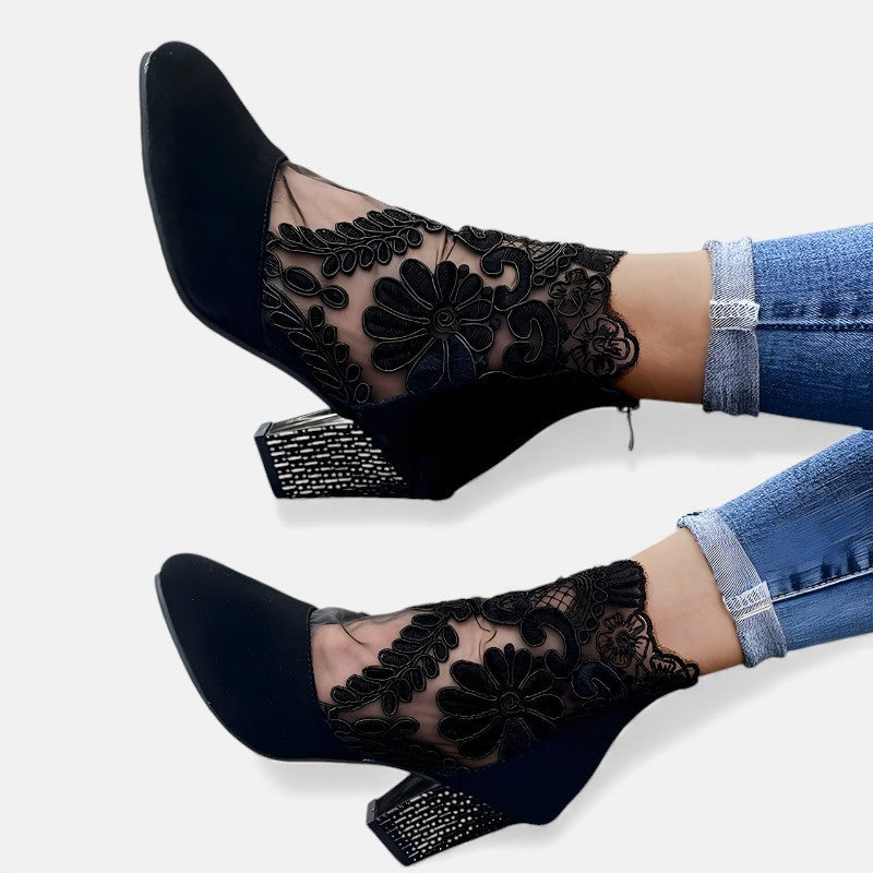 A woman wearing wine block-heel shoes with a sheer black floral-lace ankle overlay and a crystal-set heel
