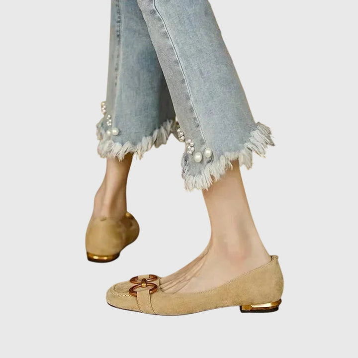 A pair of black slip-on flats with a polished gold ring detail across the toe.
