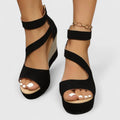 A woman in a summer dress wearing black crossover-strap heeled sandals, standing with easy confidence.