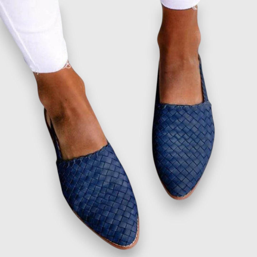 A woman wearing warm brown woven pointed-toe slingback flats with white cropped pants.