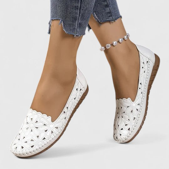 A woman wearing white floral cut-out slip-on flats on a warm, sunny day.